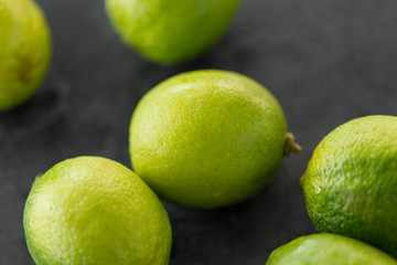 Fototapeta na wymiar food, healthy eating and vegetarian concept - close up of whole limes on slate table top