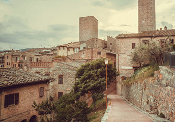 Streets and gardens of Italian medieval town with roofs of mansions at evening landscape of Tuscany. Green countryside in province of Italy