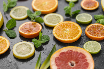 food, healthy eating and vegetarian concept - close up of grapefruit, orange, pomelo and lime slices on slate stone table top