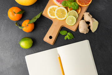 food, healthy eating and vegetarian concept - close up of citrus fruits, wooden cutting board and notebook on slate table top