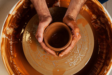 close up dirty hands of a man woman potter, creating an clay earthen jar pot on the potter's wheel...