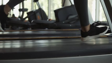 Closeup footage of woman's feet in snakers running on a treadmill in fitness club. Blonde woman in grey leggings and sport bra working out at gym - Powered by Adobe