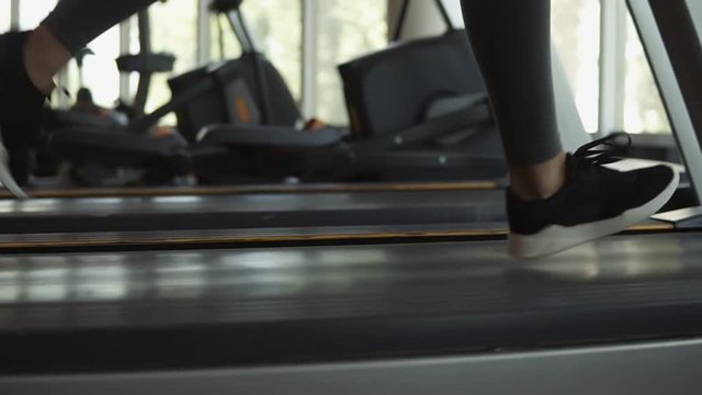 Closeup Footage Of Woman's Feet In Snakers Running On A Treadmill In Fitness Club. Blonde Woman In Grey Leggings And Sport Bra Working Out At Gym