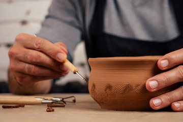 male master potter in apron sculpts a deep bowl of brown clay on a Potter's wheel In workshop on...
