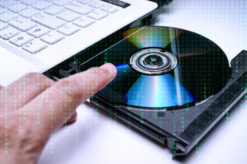 DVD Disk on the white Laptop DVD ROM Tray with a Man Hand. A Piracy conceptual image of burning data into DVD Disk