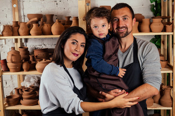 Young happy caucasian family with son working on potter shop .beautiful mother with dad and little boy making ceramic pot on the pottery art class workshop.love , care and tenderness