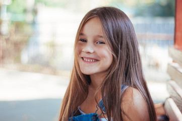 Little girl cheerful, laughs and sits on a bench in the park summer