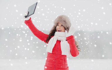 people, technology and leisure concept - happy woman in winter fur hat with tablet pc computer outdoors