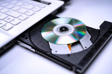 DVD Disk on the white Laptop DVD ROM Tray with a Man Hand. A Piracy conceptual image of burning data into DVD Disk