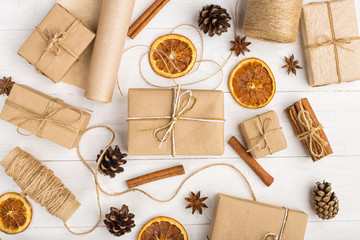 Gifts from craft paper, dried orange, cinnamon, pine cones, anise on a white table. The original decor for Christmas.