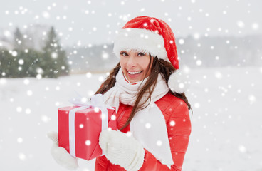 holidays and people concept - happy woman in santa hat with chrismas gift outdoors in winter