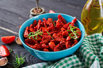 Sun dried tomatoes with herbs and garlic in  bowl on wooden table. Italian food.