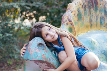 Little cute girl sitting on a dinosaur statue in the park summer