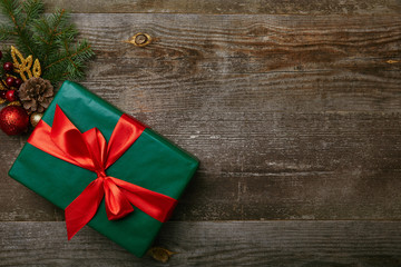 top view of wrapped green present with red ribbon and christmas toys on wooden background