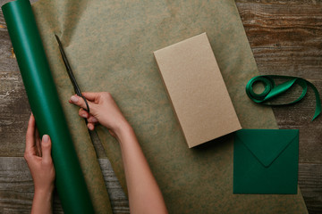 partial view of woman cutting wrapping paper with scissors on wooden surface with gift and envelope
