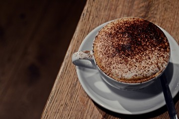 Cup of cappuccino with chocolate on top. Cappuccino drink isolated on wooden background. Hygge...