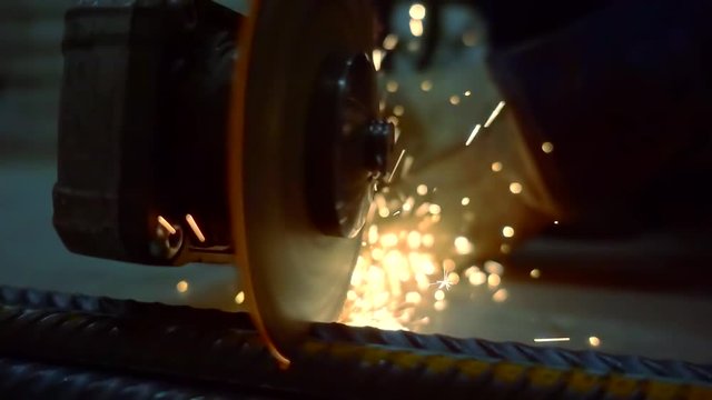 Factory worker cutting armature in pieces with angle grinder indoor.