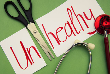 Unhealthy inscription. Stethoscope and scissors on green background. Hand writted red inscription....