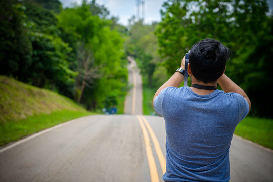 Photographer man taking photo with camera on Mountain Street. Traveler man standing on country road taking photo landscape beautiful location. Tourist man Travel concept