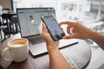 Business man hand holding smart phone touch or typing with coffee cup and laptop on table in cafe. Man drinking coffee using mobile phone. freelance blogger working, technology lifestyle concept.