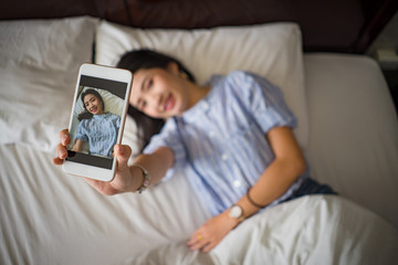 young happy woman taking selfie with mobile phone in bedroom morning.