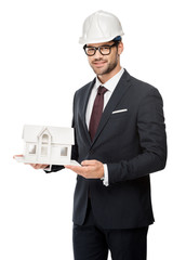 young male architect in hard hat showing miniature house isolated on white