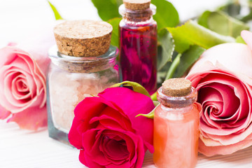Fototapeta na wymiar Spa and wellness setting with rose flower, sea salt, oil in a bottle on wooden white background