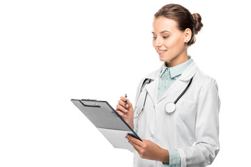 happy young female doctor in medical coat writing in clipboard isolated on white