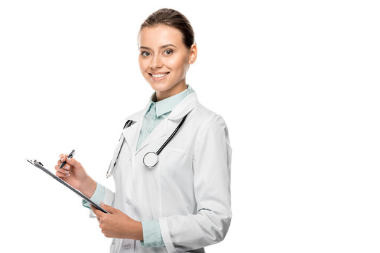 Smiling Young Female Doctor In Medical Coat Writing In Clipboard Isolated On White