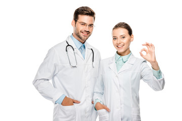 beautiful female doctor showing ok sign while her male colleague standing near with stethoscope isolated on white