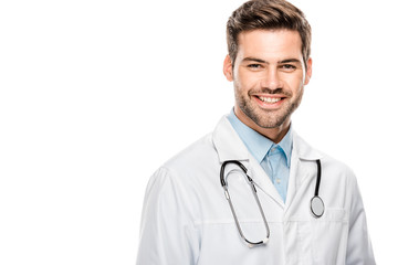 happy male doctor in medical coat with stethoscope over neck looking at camera isolated on white