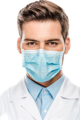 serious young male doctor in medical mask looking at camera isolated on white