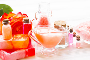 Spa and wellness setting with rose flower, sea salt, oil in a bottle on wooden white background