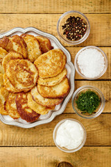 metal plate with delicious potato pancakes on an old wooden table with bowls full of additions in the kitchen