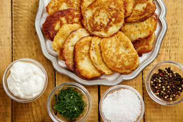 metal plate with delicious potato pancakes on an old wooden table with bowls full of additions in the kitchen
