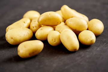 lots of young and fresh potatoes on a black wooden table in the kitchen
