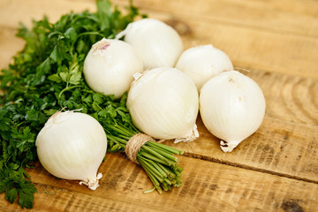 white fresh onion and a bunch of parsley on an old wooden kitchen table