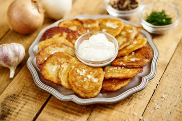 metal plate with delicious potato pancakes on an old wooden table with garlic onions and toppings in the kitchen