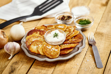 metal plate with delicious potato pancakes on an old wooden table with bowls full of additions in the kitchen