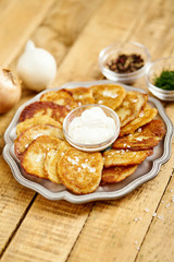 metal plate with delicious potato pancakes on an old wooden table with garlic onions and toppings in the kitchen