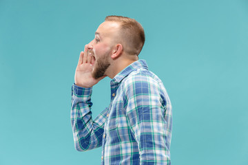 Do not miss. Young casual man shouting. Shout. Crying emotional man screaming on blue studio background. male half-length portrait. Human emotions, facial expression concept. Trendy colors