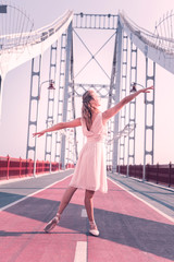 Beautiful movements. Joyful positive woman looking at her hand while dancing on the bridge © Viacheslav Yakobchuk