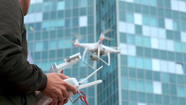 Young man flying quadro drone with modern white RC transmitter. Male filmer controlling drone over RC radio controller. Man filming with drone camera near industrial city and high-tech building