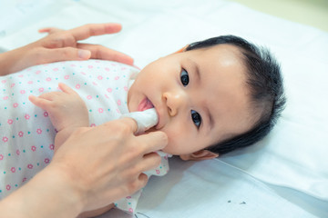 Mother use finger to clean asian baby tongue with clean gauze.