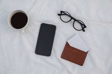 Naklejka premium Smart phone on the bed with coffee cup and pocket blank card.