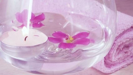 Fototapeta na wymiar Romantic composition with a candle and violet flowers floating in a bowl of water.The concept of Spa,cosmetic,procedure,treatment.
