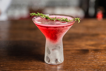 A photo of a red alcoholic drink in a frozen cocktail glass, garnished with thyme.