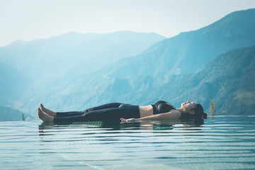 Beautiful Attractive Asian woman practice yoga Dead Body or Savasana on the pool above the Mountain...