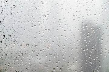 Rain drops on window glasses surface with cloudy background.