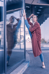 My flexibility. Joyful nice woman putting her leg on the glass door while showing her flexibility © Viacheslav Yakobchuk